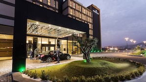 A modern hotel entrance with a glass facade, a landscaped garden, and a parking area. - Dedeman Cizre (Cizre)