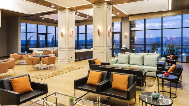 A spacious lobby with modern furniture, large windows offering city views, and a high ceiling with recessed lighting. - Dedeman Cizre (Cizre)
