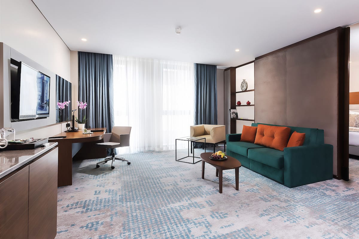 A modern hotel room with a bed, a sofa, a desk, and a TV.