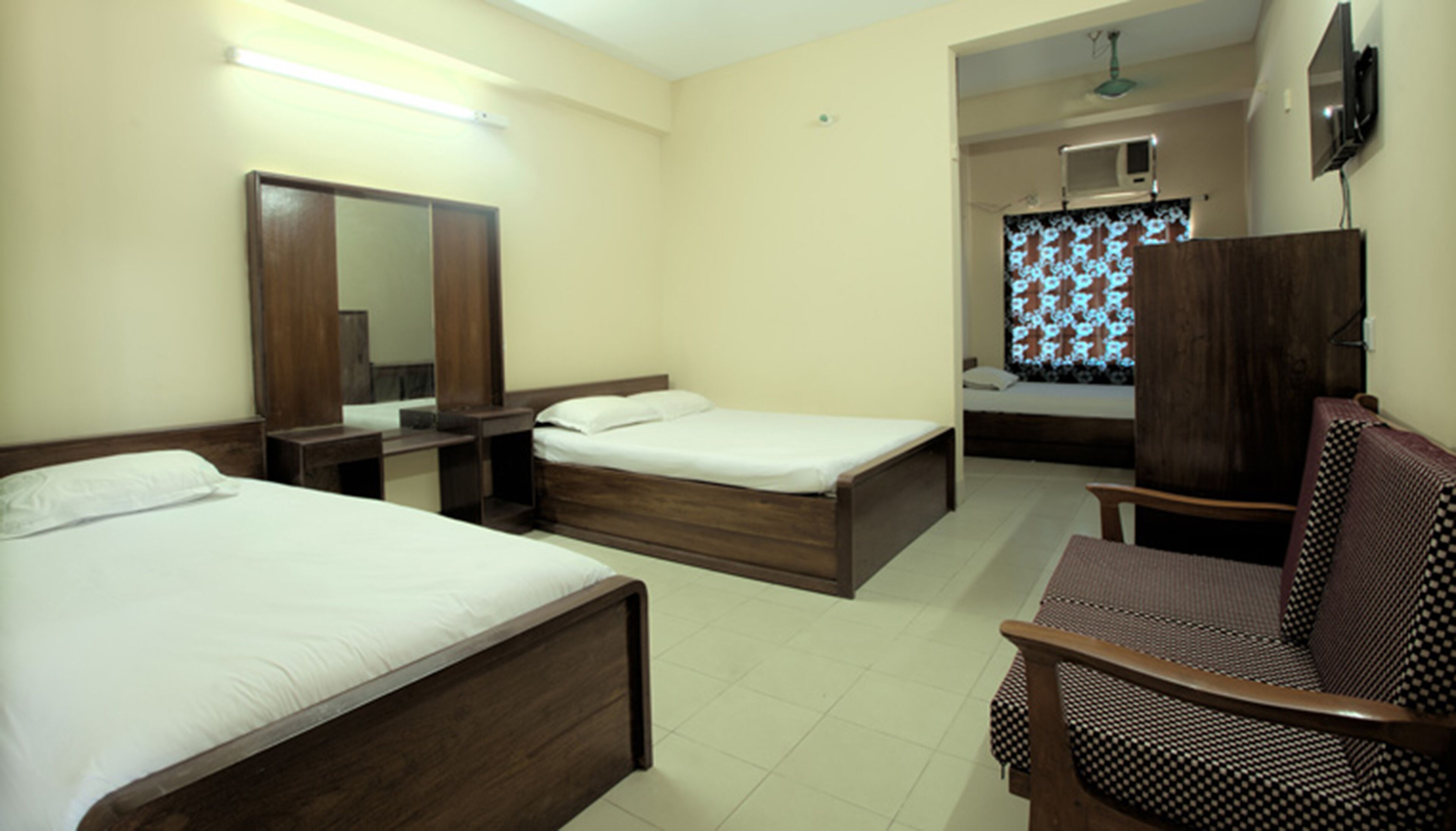A hotel room with two single beds, a desk, a chair, a wardrobe, and a television.