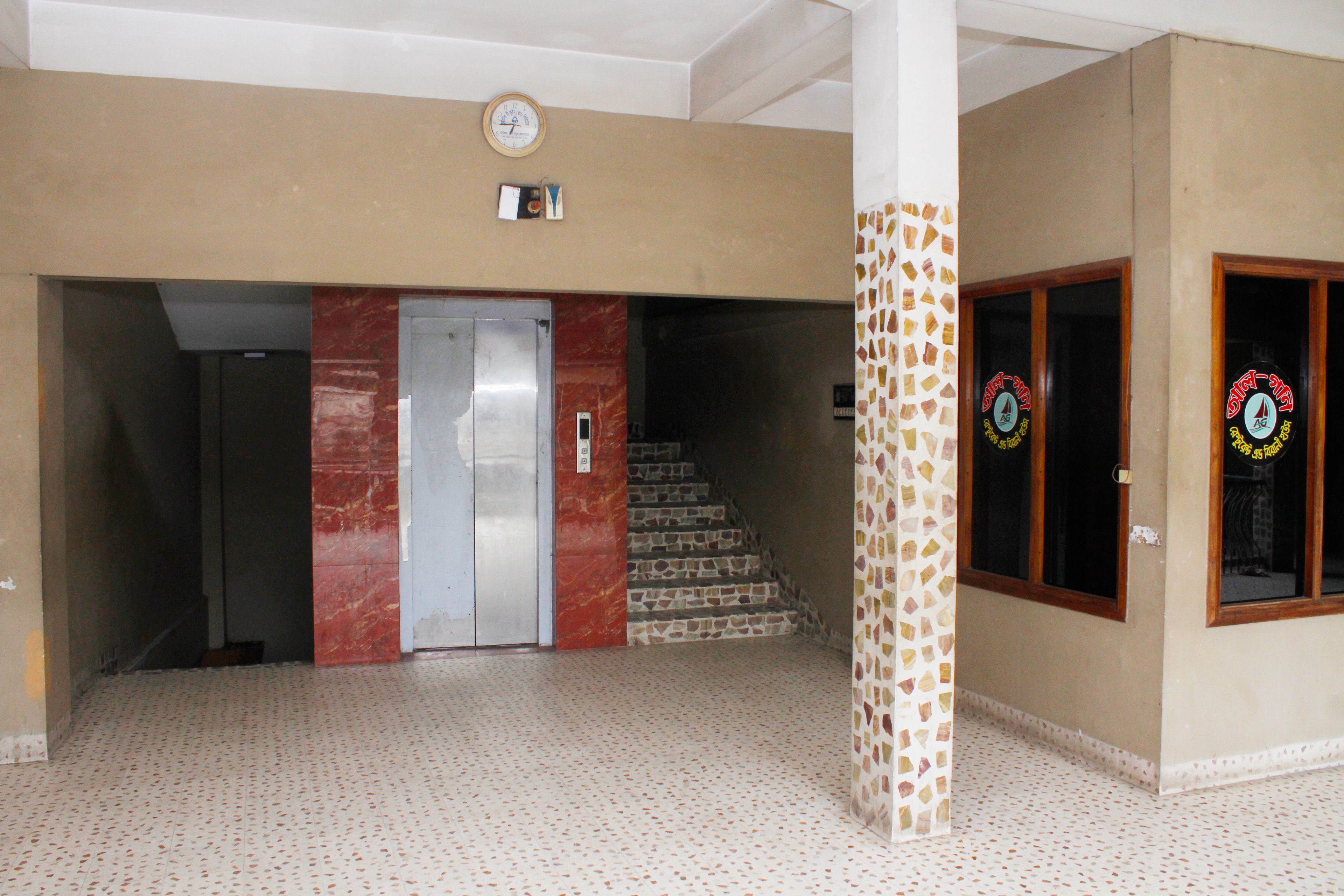 A hotel lobby with a marble elevator, a staircase, and a mosaic wall.