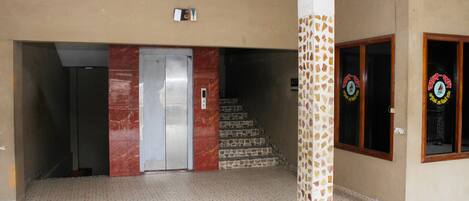 A hotel lobby with a marble elevator, a staircase, and a mosaic wall.