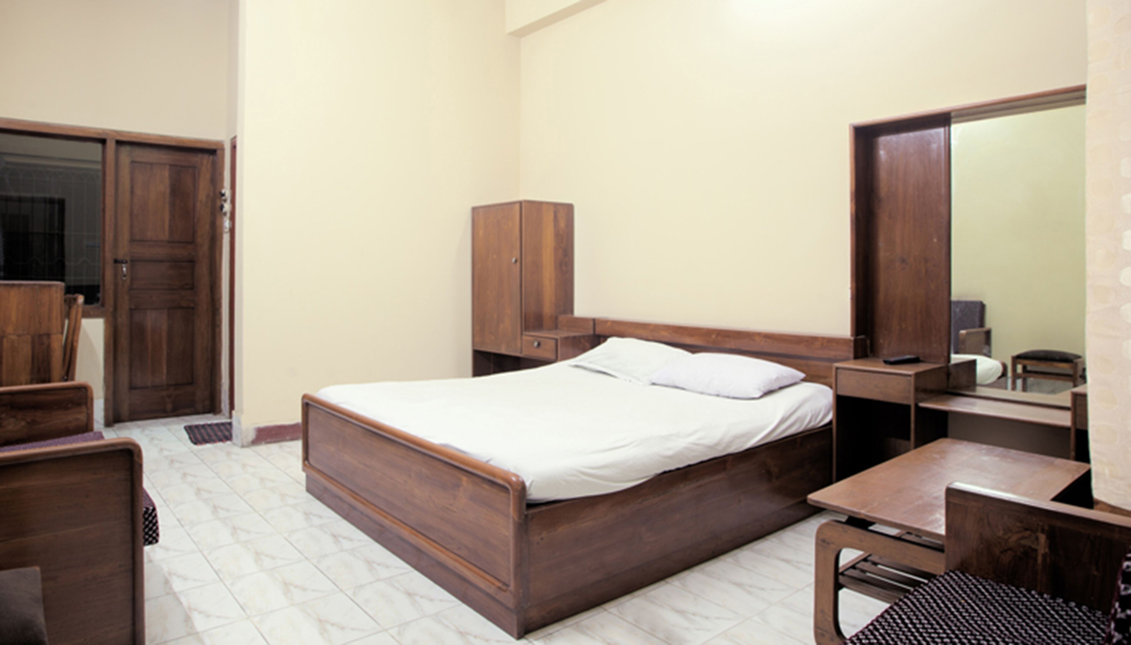Een slaapkamer met een houten bed, een houten garderobe, een bureau, een stoel en een spiegel.