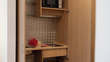Una cocina compacta con un microondas en un estante, un lavabo y un salpicadero de azulejos.