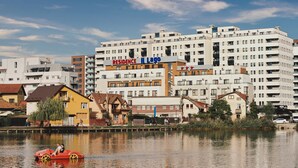 A multi-story building with a sign reading "RESIDENCE Il Lago" and a red car on a body of water in front.