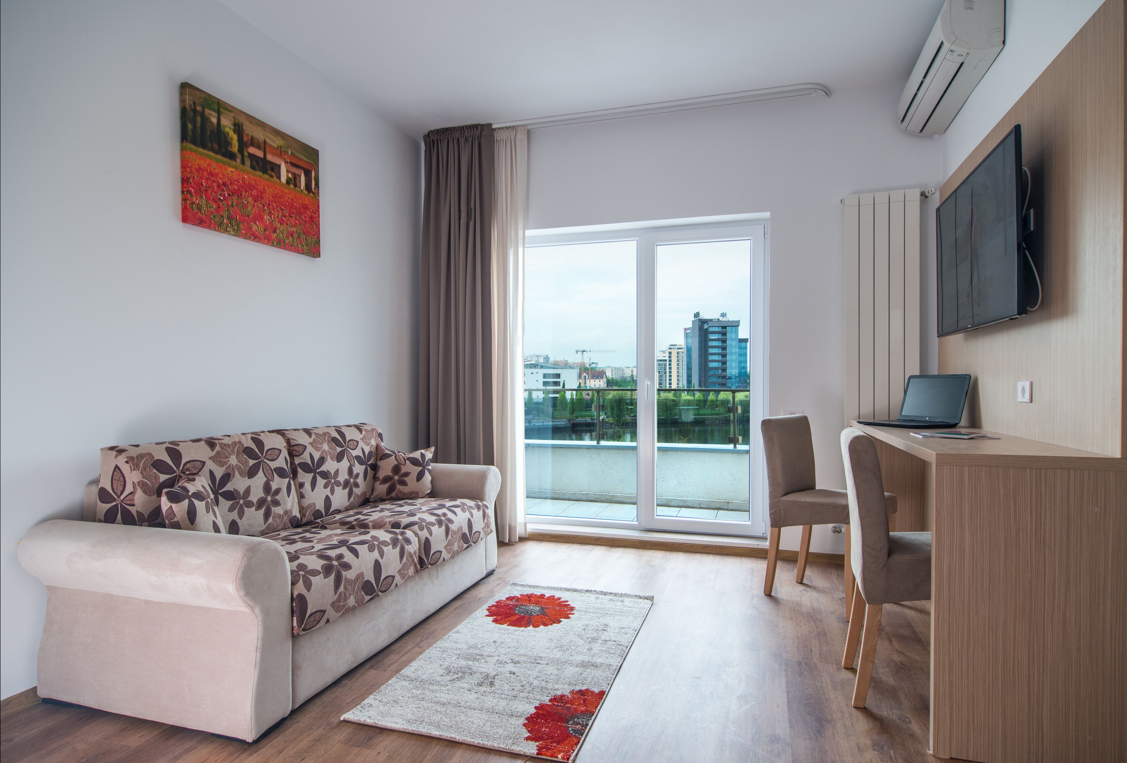 En moderne stue med sofa, skrivebord og stort vindue med udsigt over byen.