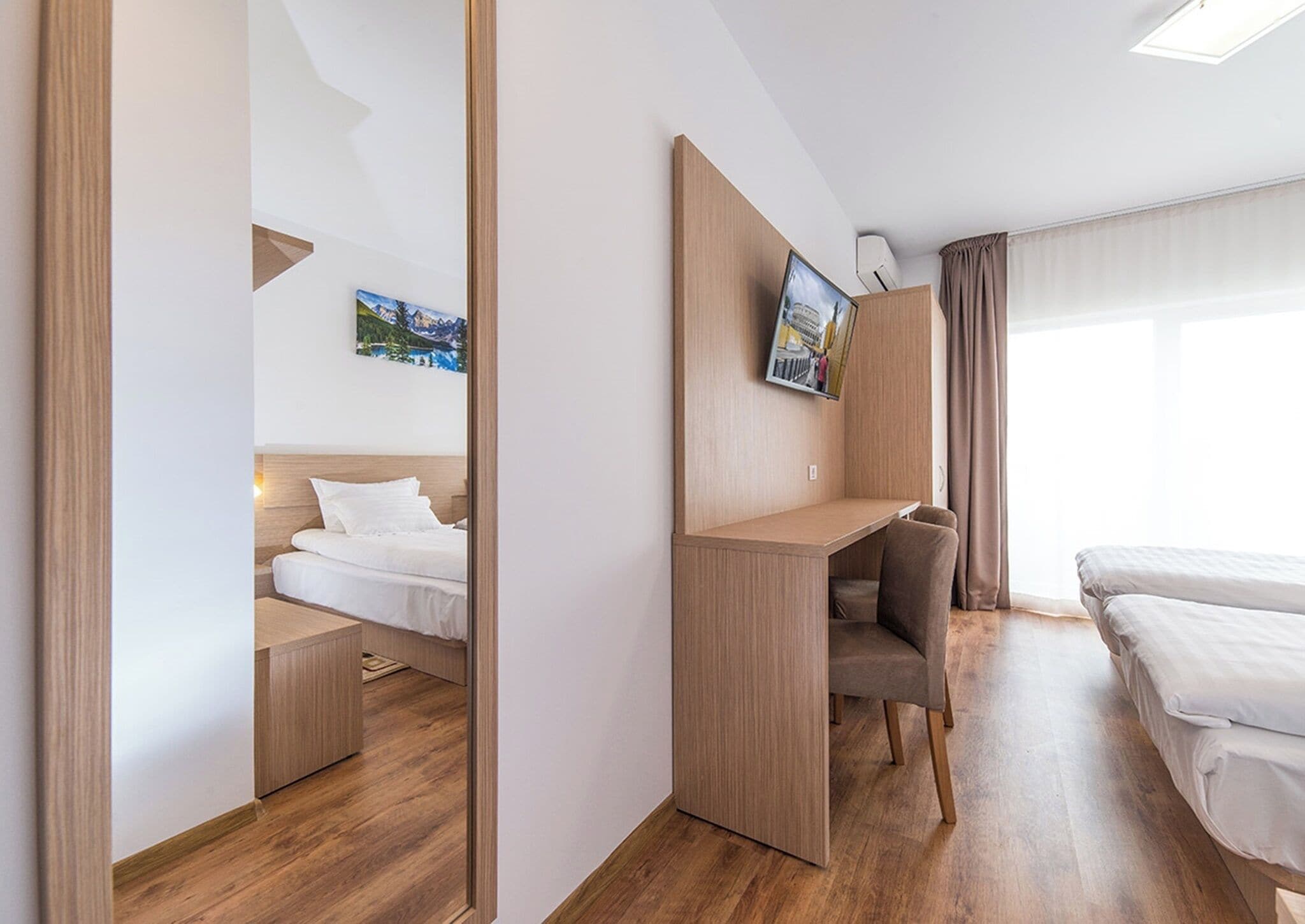 A hotel room with a bed, a desk, a chair, a TV, and a window with curtains.