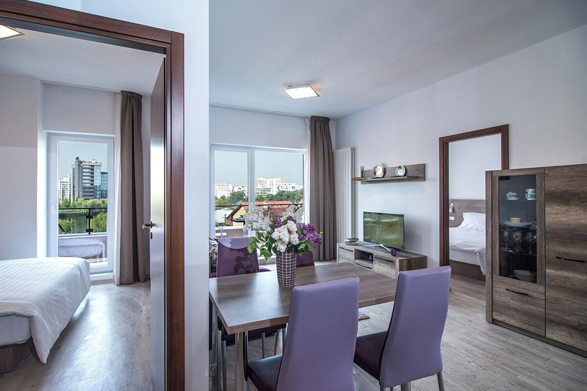 A hotel room with a bed, a dining area with a table and chairs, a TV, and a wardrobe.