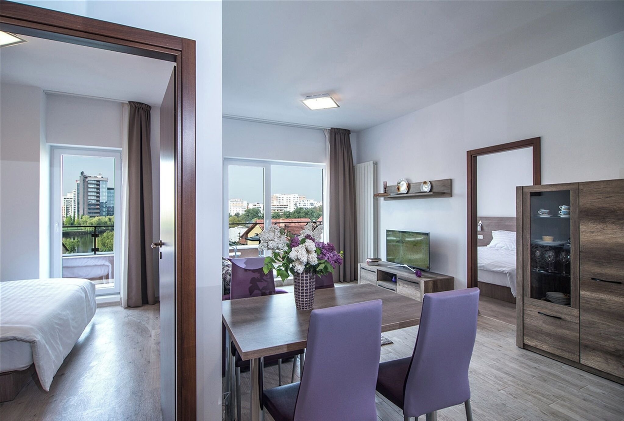 Una habitación de hotel con una cama, zona de comedor con mesa y sillas, televisor y armario.