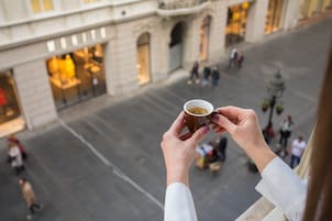 A person holding a cup, overlooking a city street with shops and pedestrians.