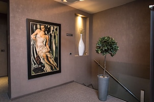 A hallway with a framed painting, a sign indicating a breakfast area, a white vase with a plant, and a tall potted plant.