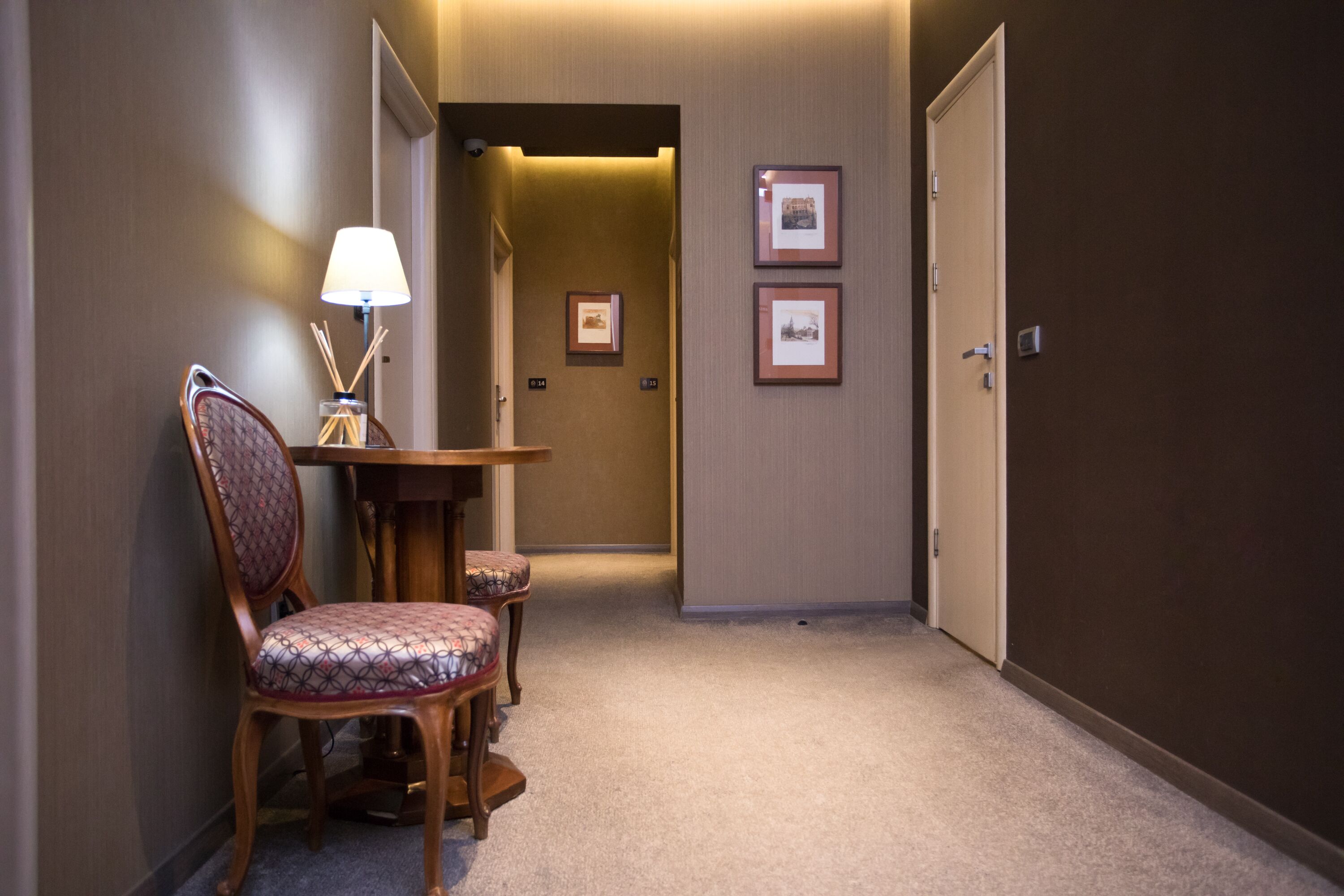 A hallway with a dining area featuring a table and chairs, framed pictures on the wall, and a door at the end.