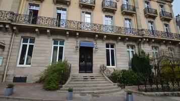 Un immeuble à plusieurs étages, doté d’une façade symétrique, de grandes fenêtres et de balcons en fer forgé noir richement décorés.