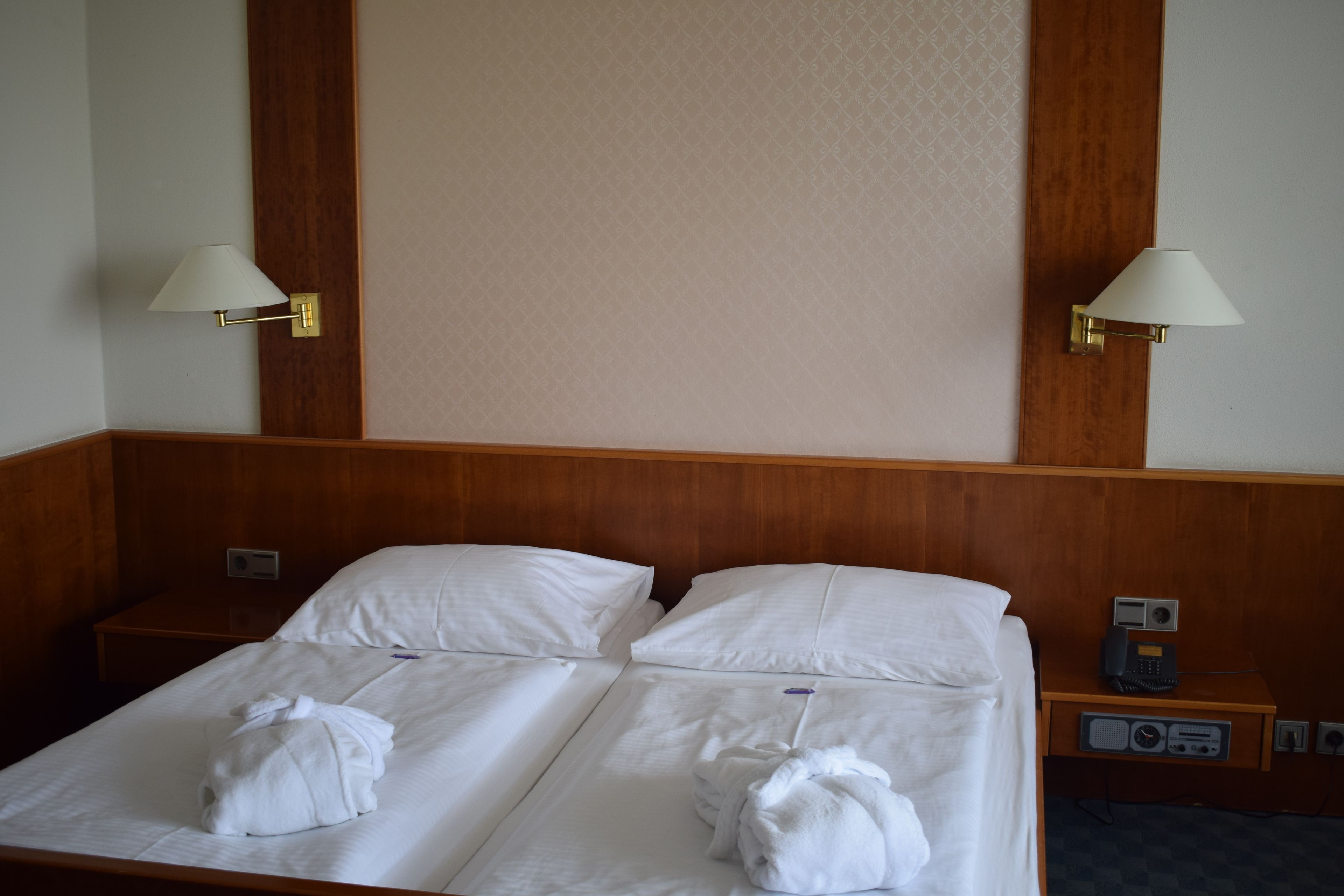 Une chambre d’hôtel avec deux lits, chacun équipé de draps et de serviettes blancs. Deux lampes murales sont fixées de chaque côté des lits.