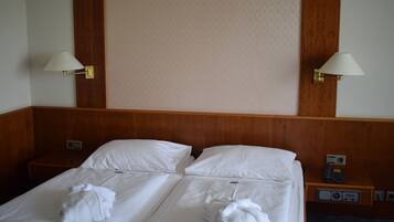 Une chambre d’hôtel avec deux lits, chacun équipé de draps et de serviettes blancs. Deux lampes murales sont fixées de chaque côté des lits.