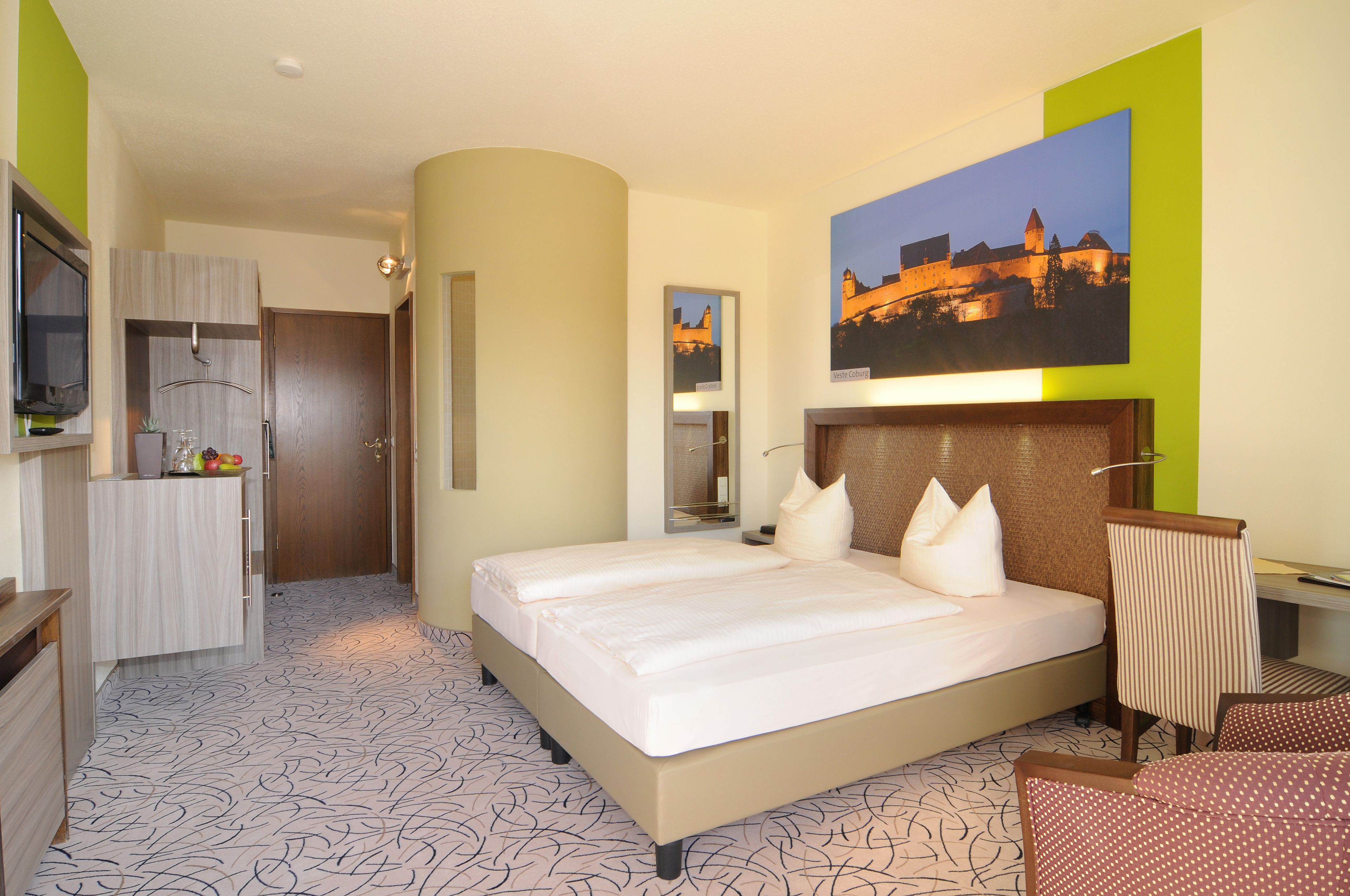 A hotel room with a large bed, a television, a desk with a chair, and a painting on the wall.