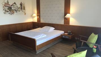 A hotel room with a wooden bed, two bedside lamps, a nightstand with a phone, and a chair with a green cushion.
