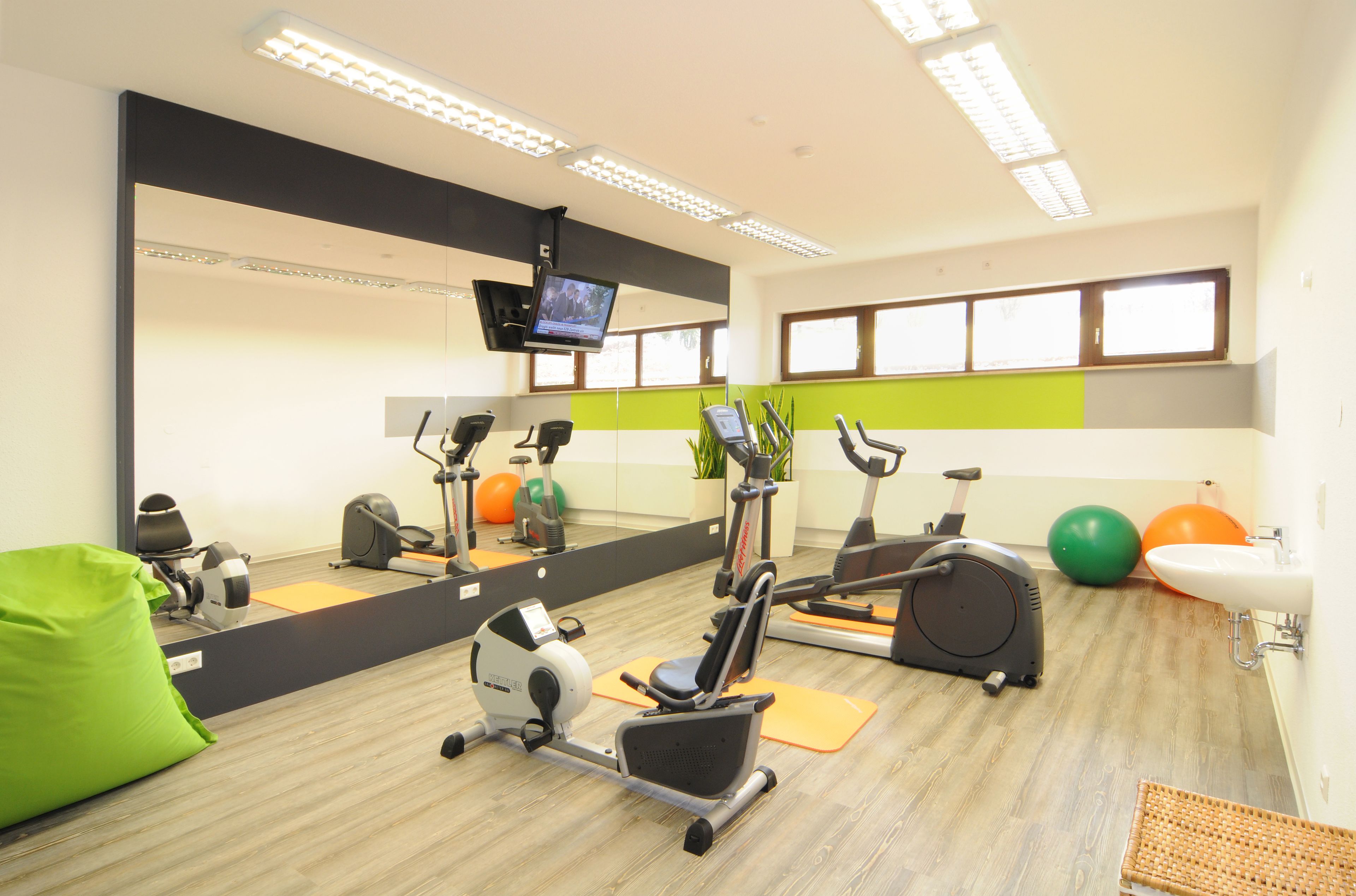 Une salle de sport équipée de matériel d’exercice, d’un miroir, d’un téléviseur et d’un lavabo.