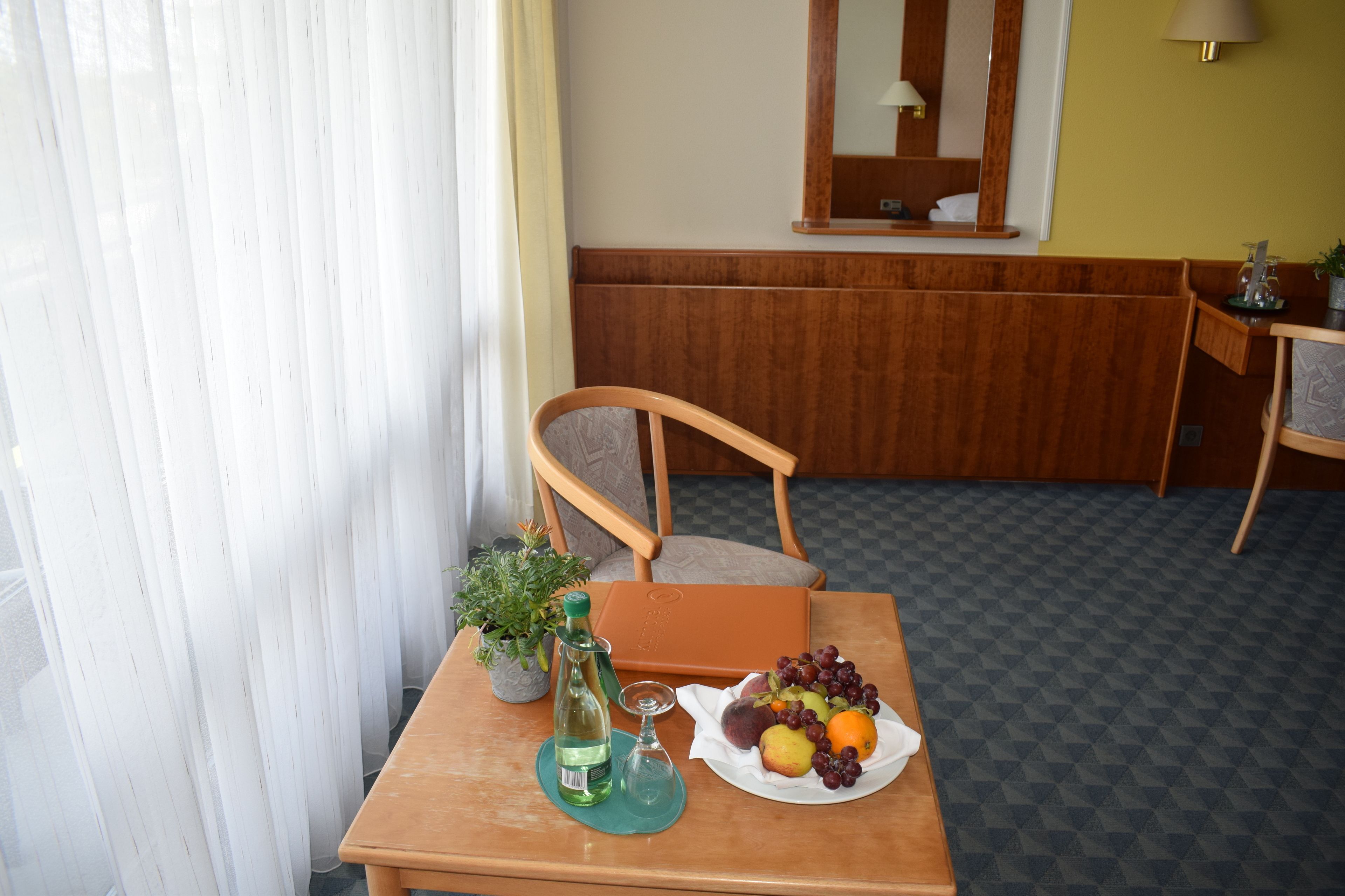 A wooden table with a bottle, glass, and a plate of fruit.