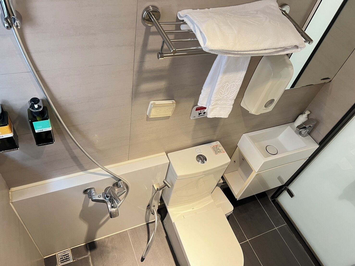 Un baño moderno con inodoro, lavamanos y ducha. Hay secamanos y dispensador de jabón.