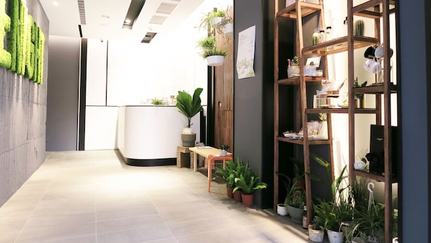 A modern reception area with a wooden reception desk, potted plants, and a shelving unit with various items. - Greenight Hotel (Taichung)