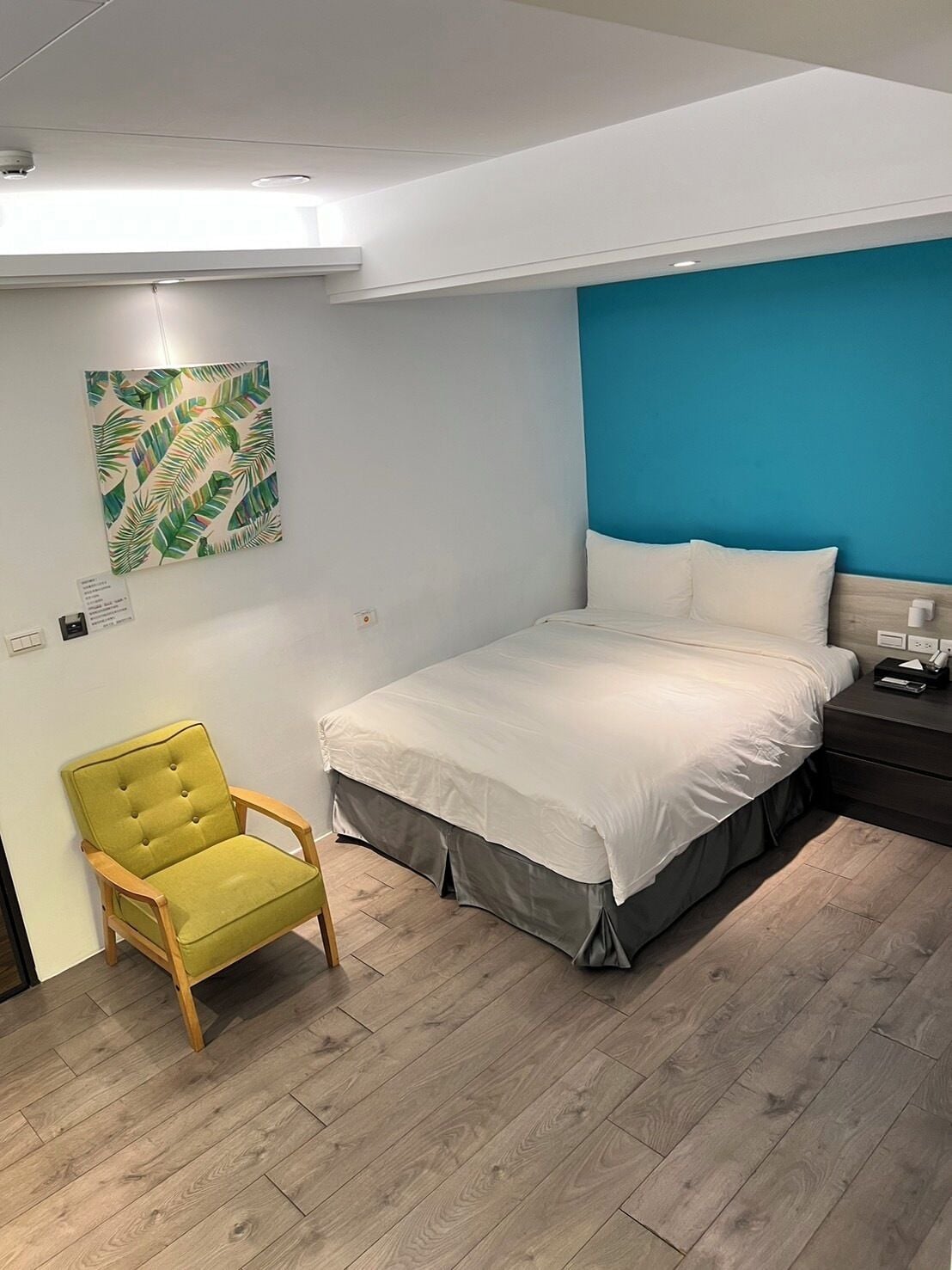 A bedroom with a bed, a chair, and a wall with a tropical leaf pattern.