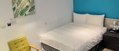 A bedroom with a bed, a chair, and a wall with a tropical leaf pattern.