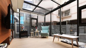 A modern living room with a large window, a blue armchair, a wooden table, and a TV mounted on the wall. - Greenight Hotel (Taichung)