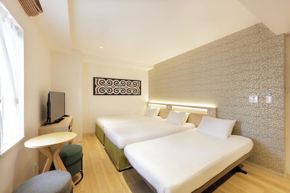 A hotel room with two beds, a desk, a chair, and a TV.