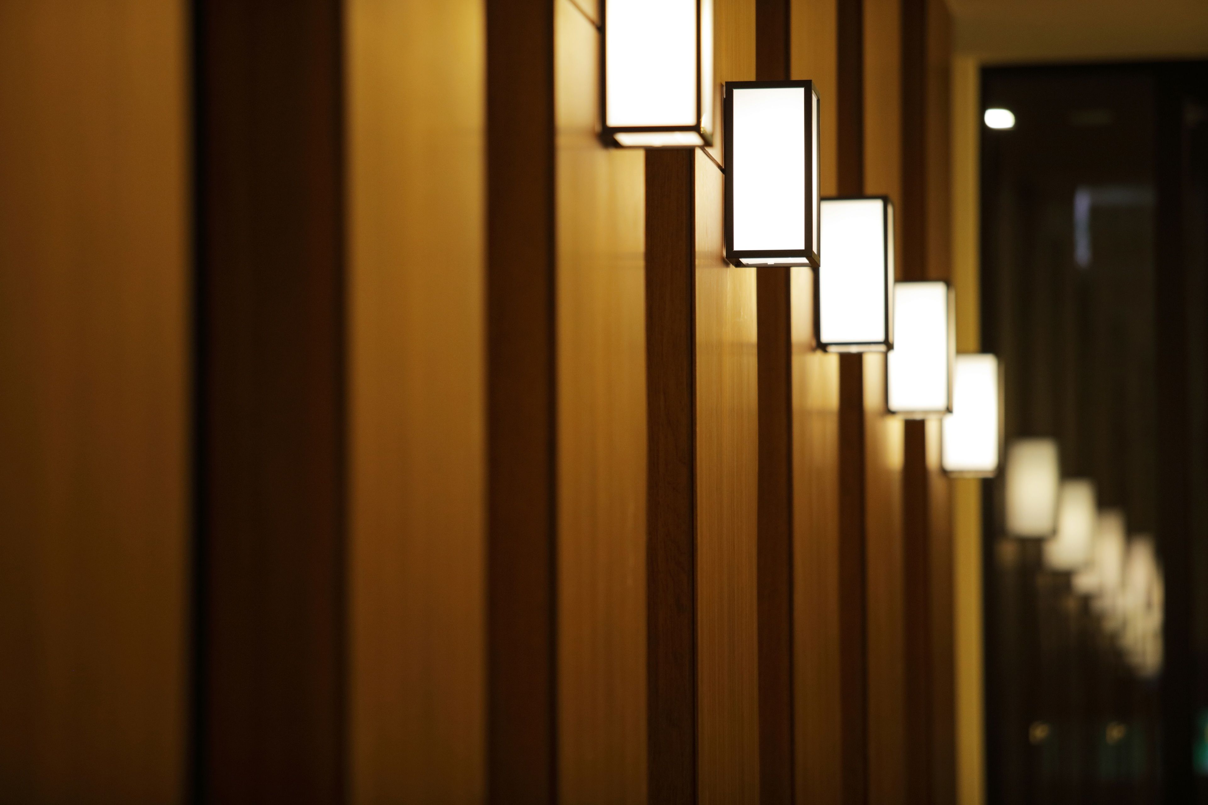 A corridor with wooden paneling and wall-mounted rectangular light fixtures.