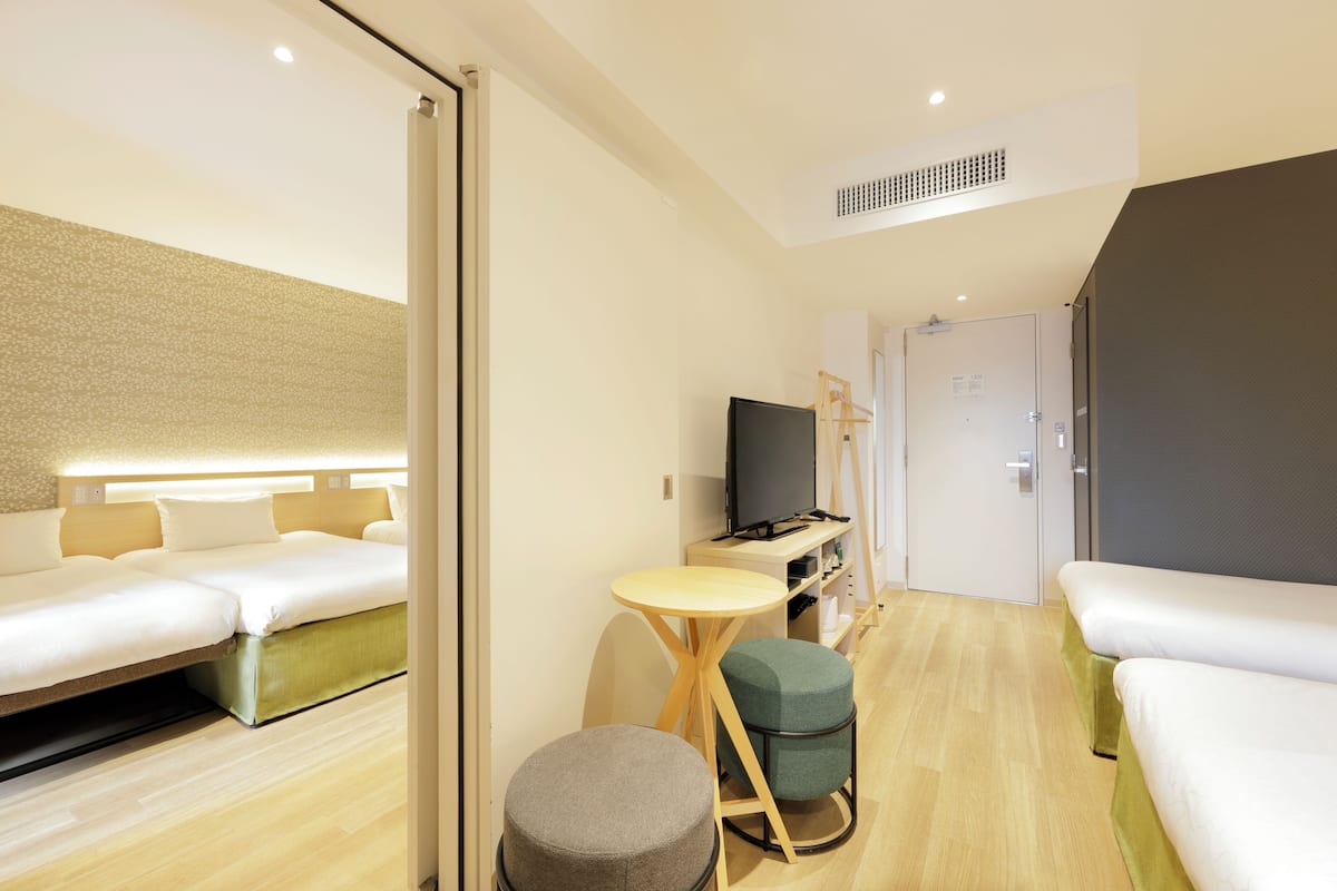 A modern hotel room with a sofa bed, a small round table, a television, and a wardrobe.
