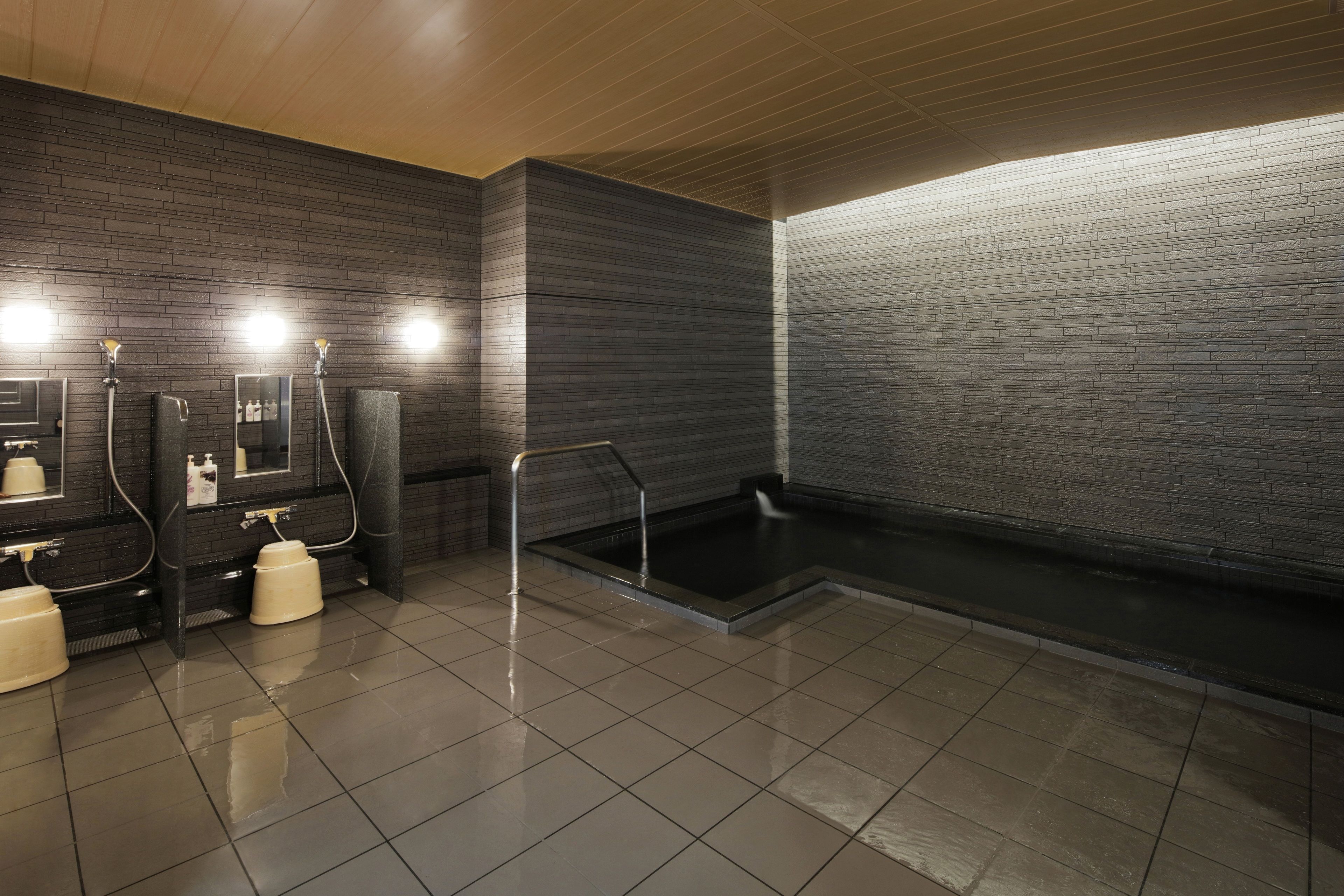Un baño moderno con pared de azulejos negros, una bañera grande y un espejo con luces arriba.