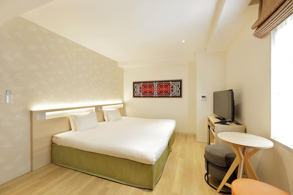 A modern hotel room with a large bed, a desk with a television, and a small table.