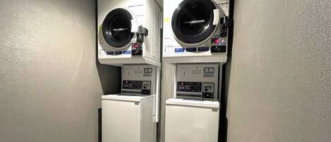 Une buanderie équipée de deux machines à laver et deux sèche-linge à chargement frontal, chacune dotée d’un panneau de commande et d’un système de paiement par pièces.