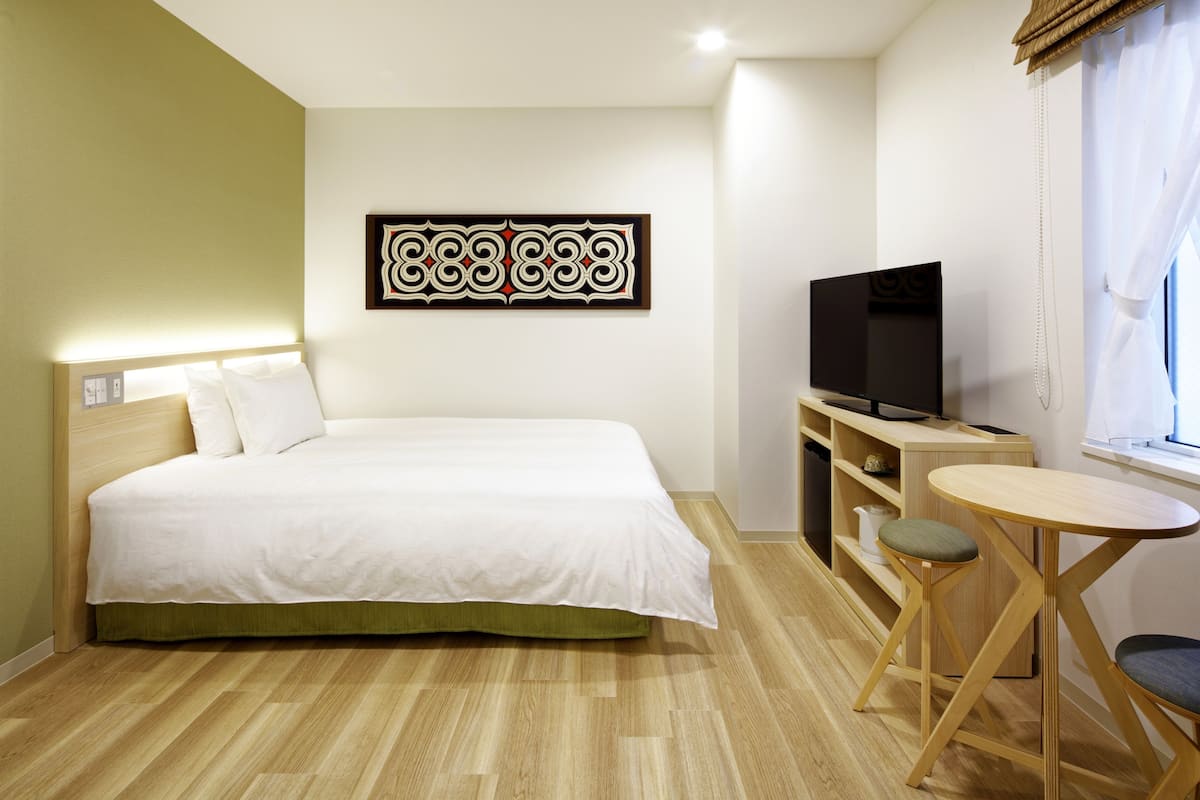 A hotel room with a bed, a TV, a small table, and a window.