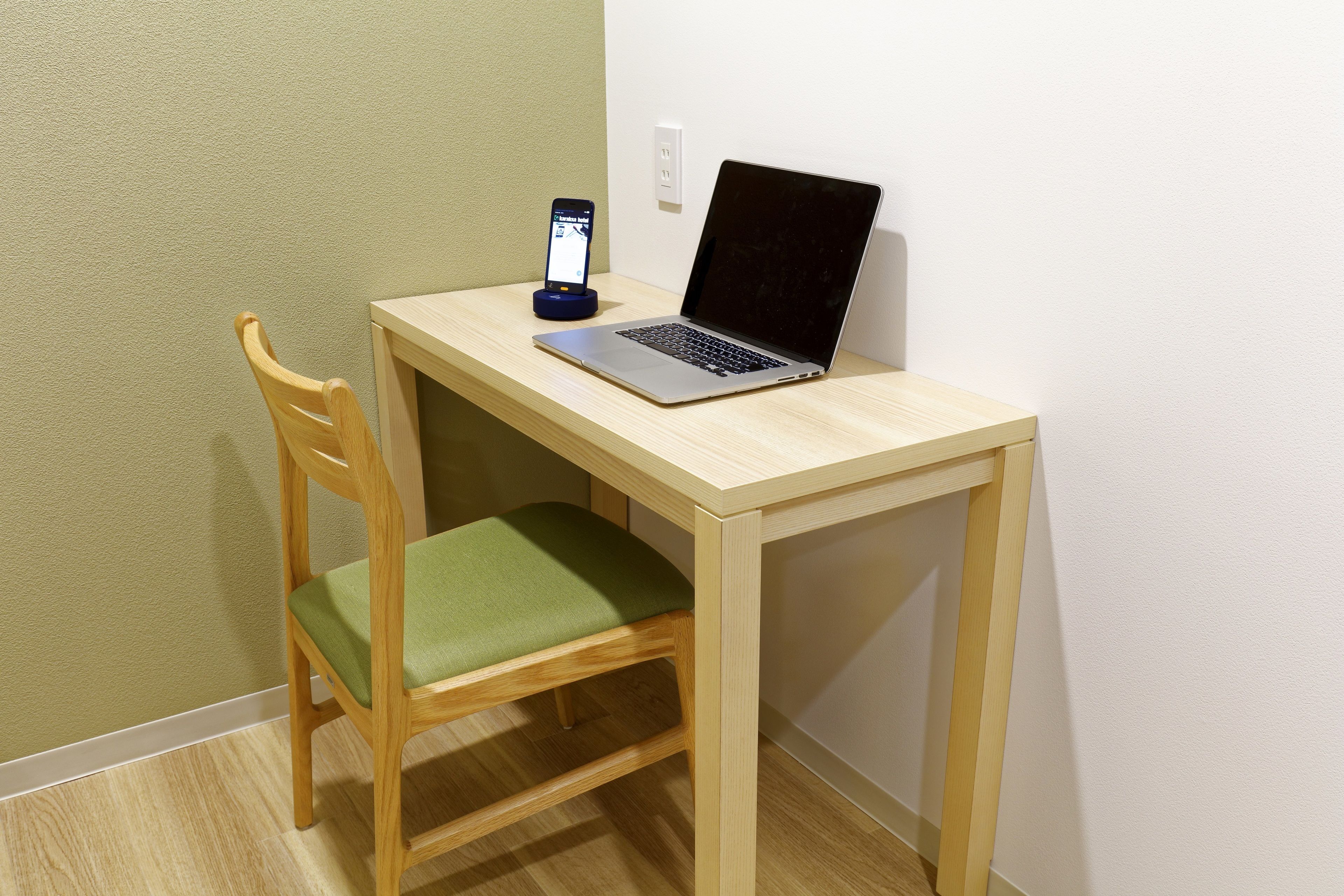 A wooden desk with a laptop and a smartphone on a charging dock.