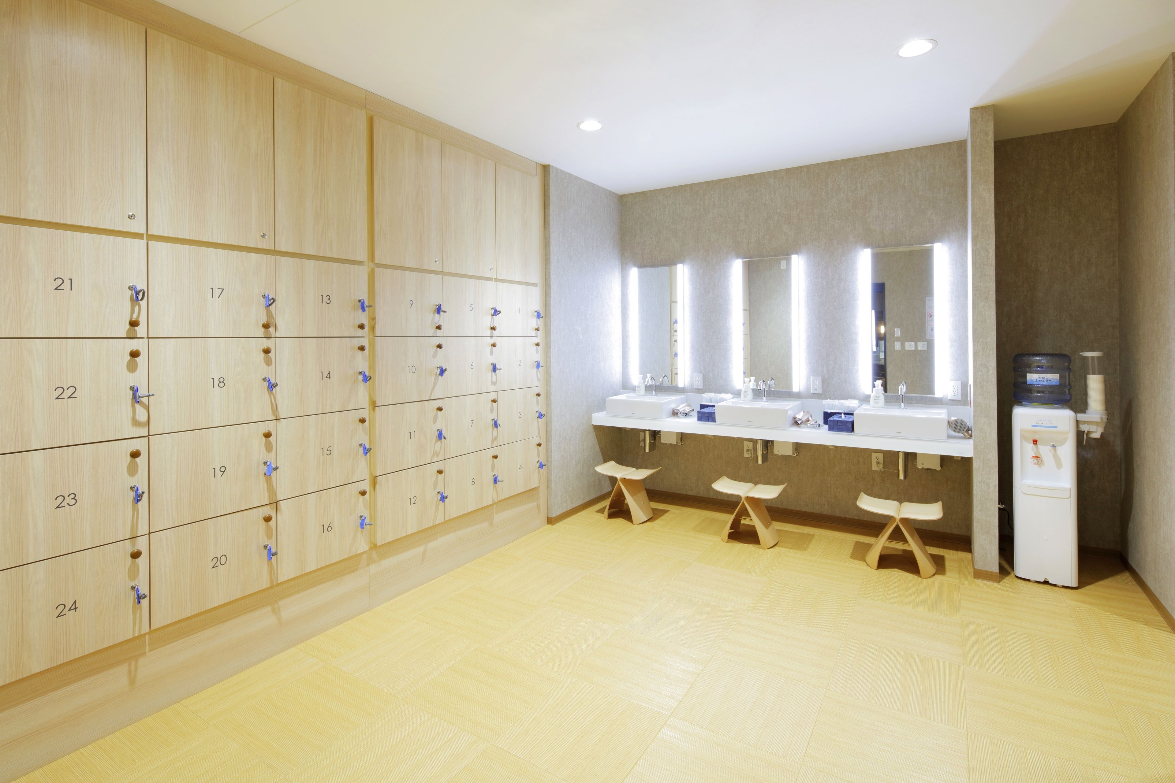Un baño de hotel con taquillas de madera, zona de lavamanos y dispensador de agua.