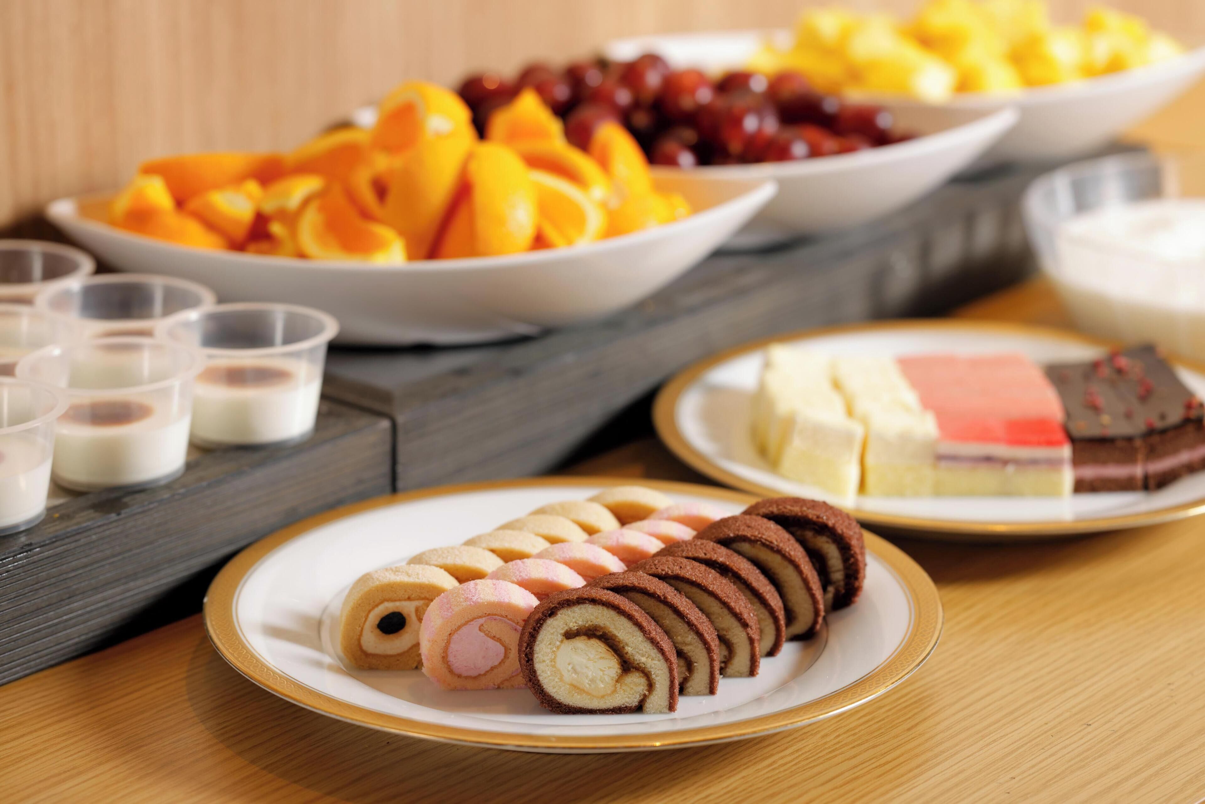 A table with various food items including sliced pastries, fruits, and desserts.