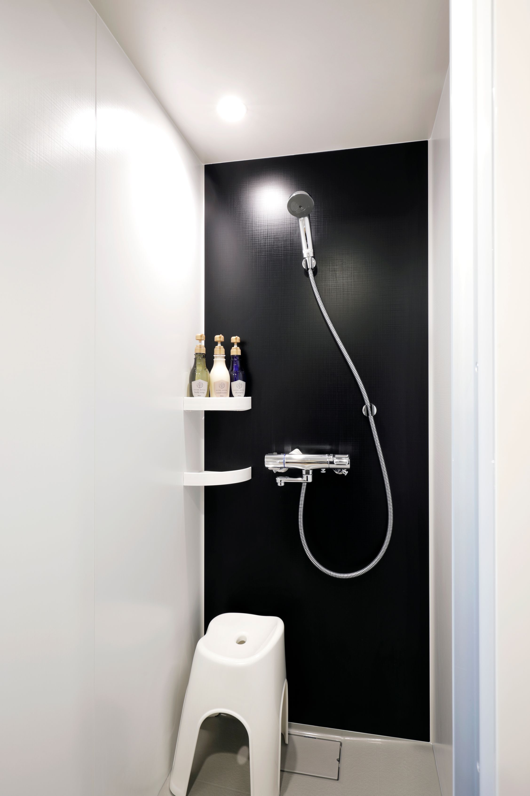 Un baño moderno con una pared negra, un inodoro blanco y una ducha con cabezal de ducha de mano.