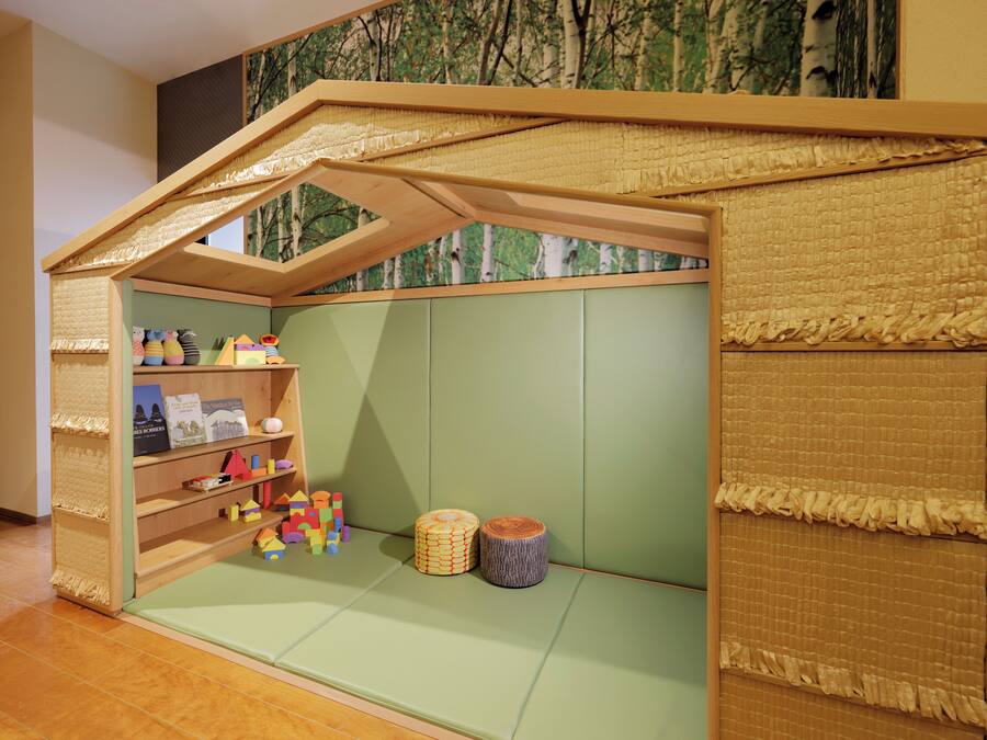 Ein Spielzimmer für Kinder mit einem Hochschlafplatz, Regalen voller Spielzeug und einer grünen Spielmatte.