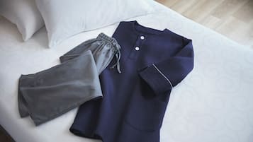 A neatly made bed with a white pillow and a blue and grey garment laid out on it.