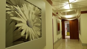 Um corredor com uma grande obra de arte floral emoldurada à esquerda, uma porta de madeira no final e piso ladrilhado.