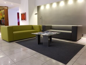 A modern lobby with a green sofa, a grey sofa, a coffee table with magazines, and a floor lamp. - Hotel Artemide (Aversa)