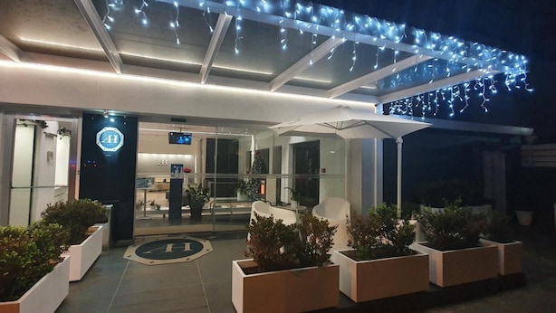 Entrada de hotel com design moderno, destacando uma porta de vidro, balcão de recepção e um painel digital.