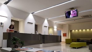 Uma área de recepção moderna, com balcão, televisão na parede e um espaço de estar com sofá e apoio para os pés.