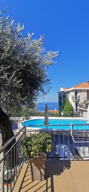 Un espace piscine offrant une vue dégagée sur la mer, un arbre et un bâtiment doté d’un toit en tuiles.