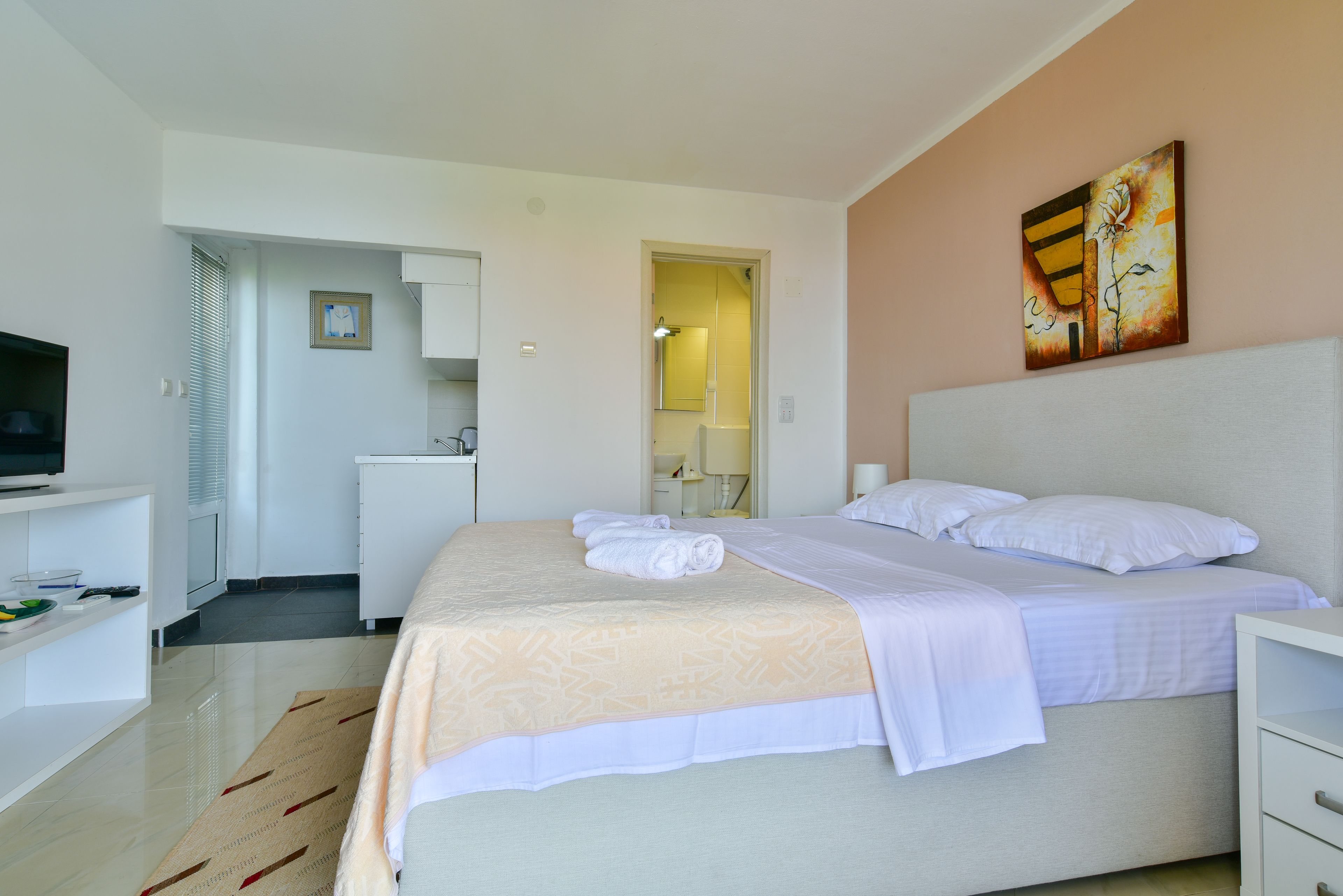 A hotel room with a bed, a TV, a desk, and a painting on the wall.