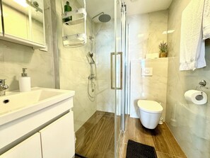 Une salle de bain moderne avec une douche à parois de verre, des toilettes blanches et un lavabo surmonté d’un miroir.