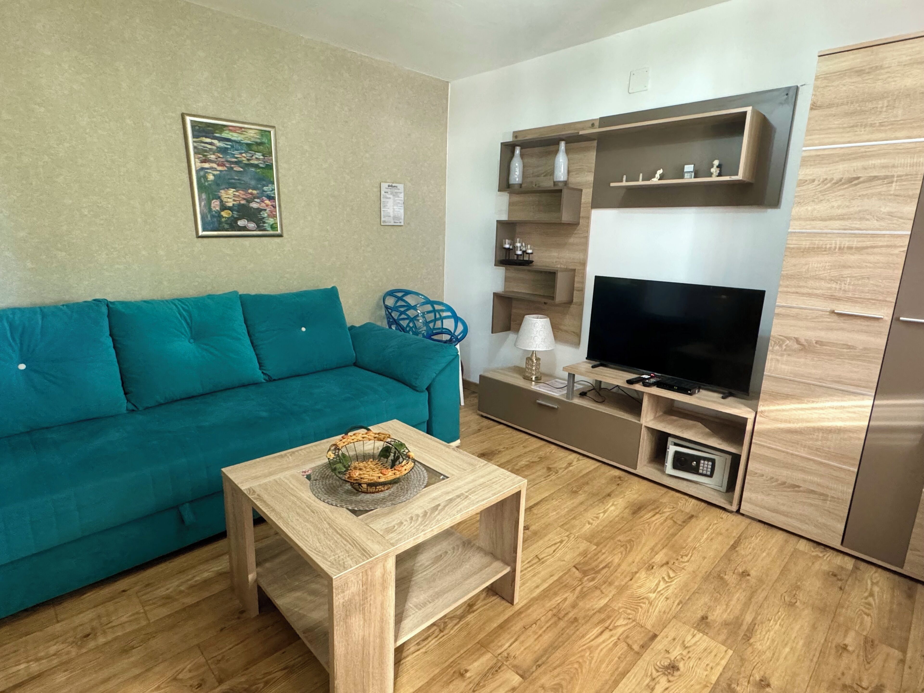 A living room with a teal sofa, a wooden coffee table, a TV, and built-in shelving with decorative items.