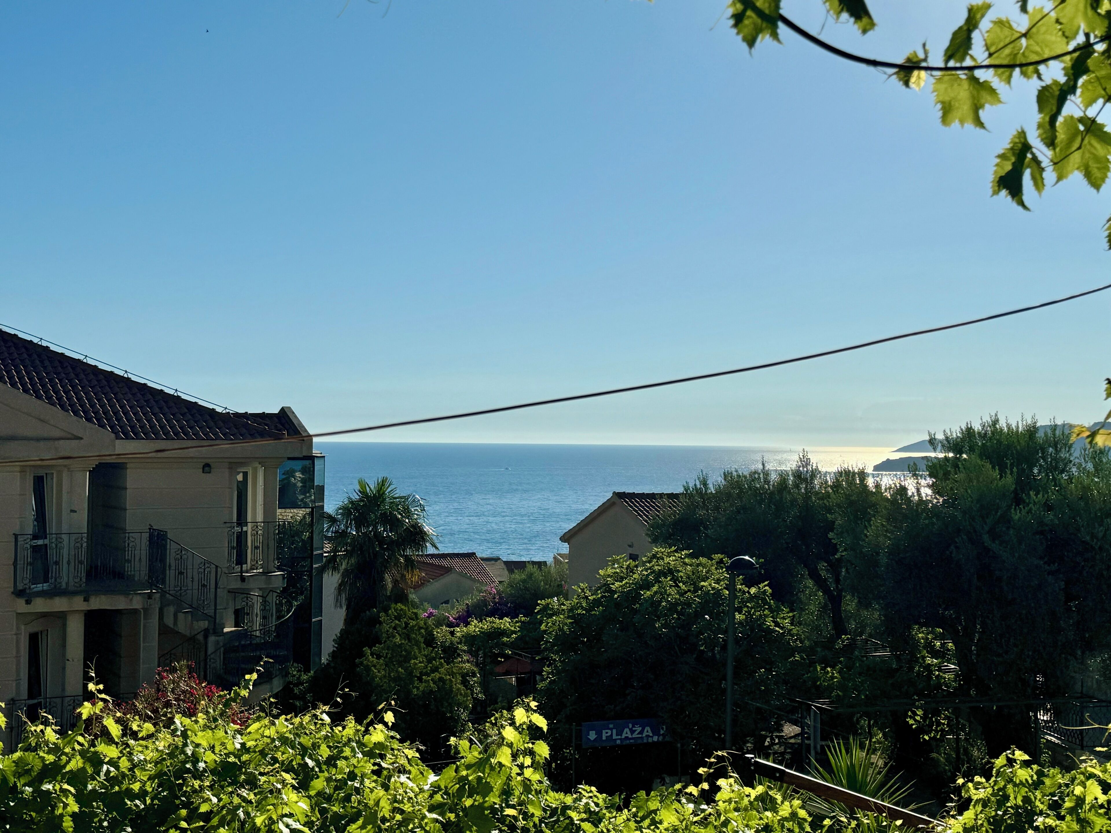 A residential area with a view of the sea, a sign indicating a plaza, and a building with a tiled roof.
